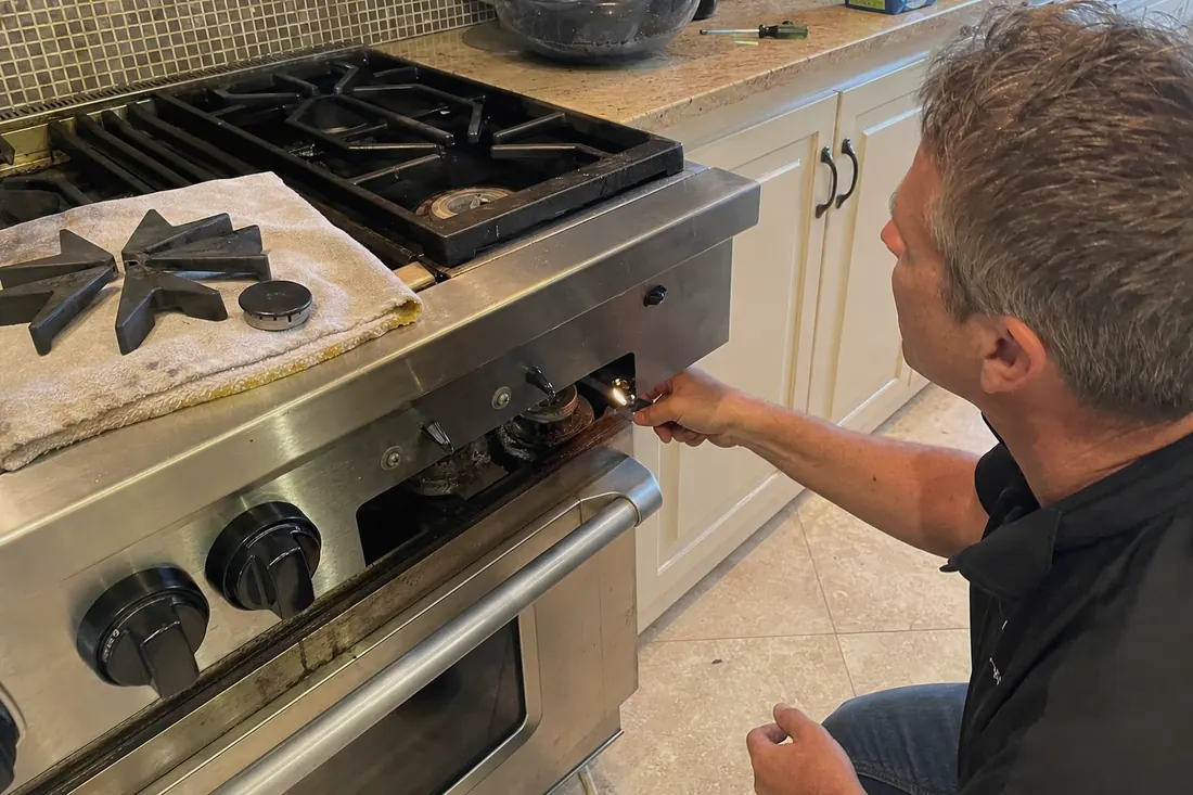 Technician checking the igniter on a dual-fuel range, one burner cap lifted off - Bertazzoni repair in Jacksonville and Northeast Florida