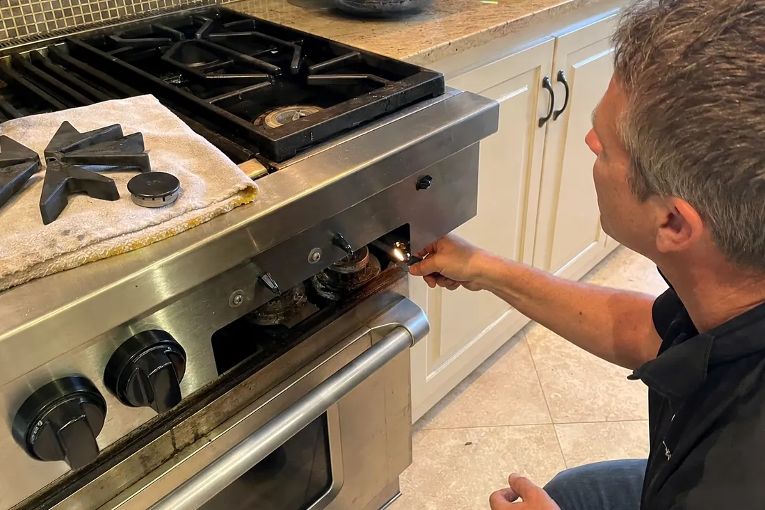 Technician checking the igniter on a dual-fuel range, one burner cap lifted off, the range front in frame - Viking repair in Jacksonville and Northeast Florida
