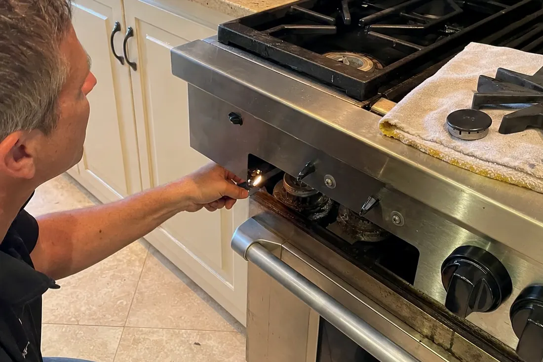 Technician checking the igniter on a dual-fuel range, one burner cap lifted off, the cast-iron grates in frame - Sub-Zero and luxury appliance repair in San Marco