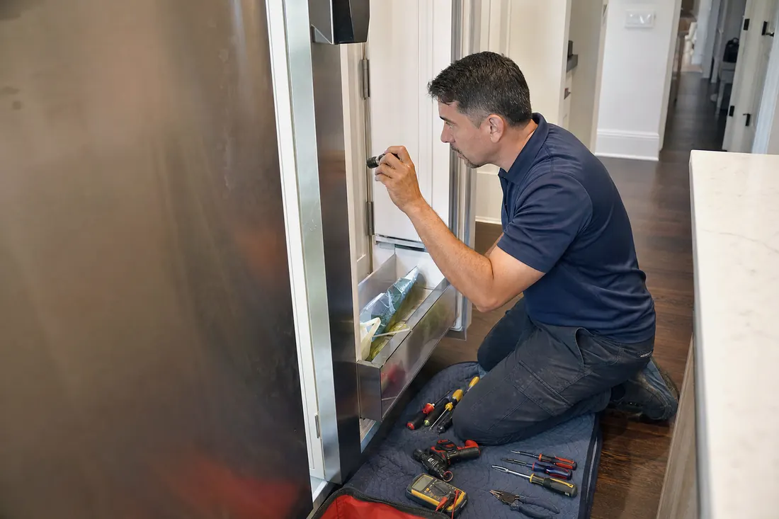 Technician checking inside an open built-in refrigerator with a flashlight, the open door in frame - Marvel repair in Jacksonville and Northeast Florida