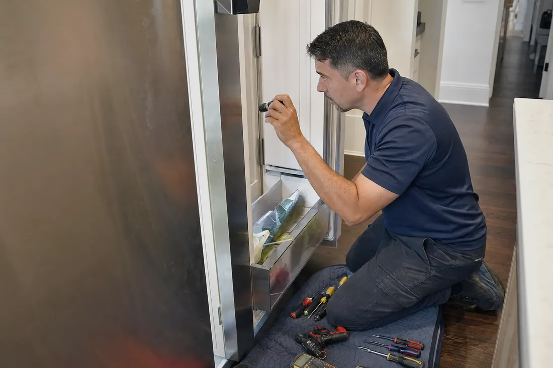 Technician checking inside an open built-in refrigerator with a flashlight, his hand steadying the door in frame - U-Line repair in Jacksonville and Northeast Florida